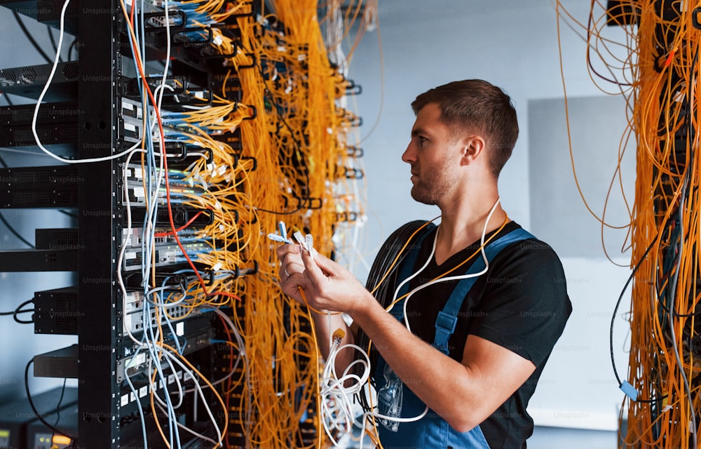 Young man in uniform feels confused and looking for a solution with internet equipment and wires in server room.