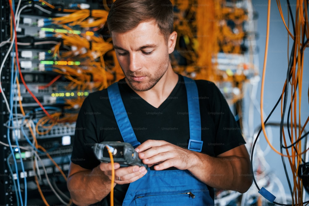 Young man in uniform have a job with internet equipment and wires in server room.