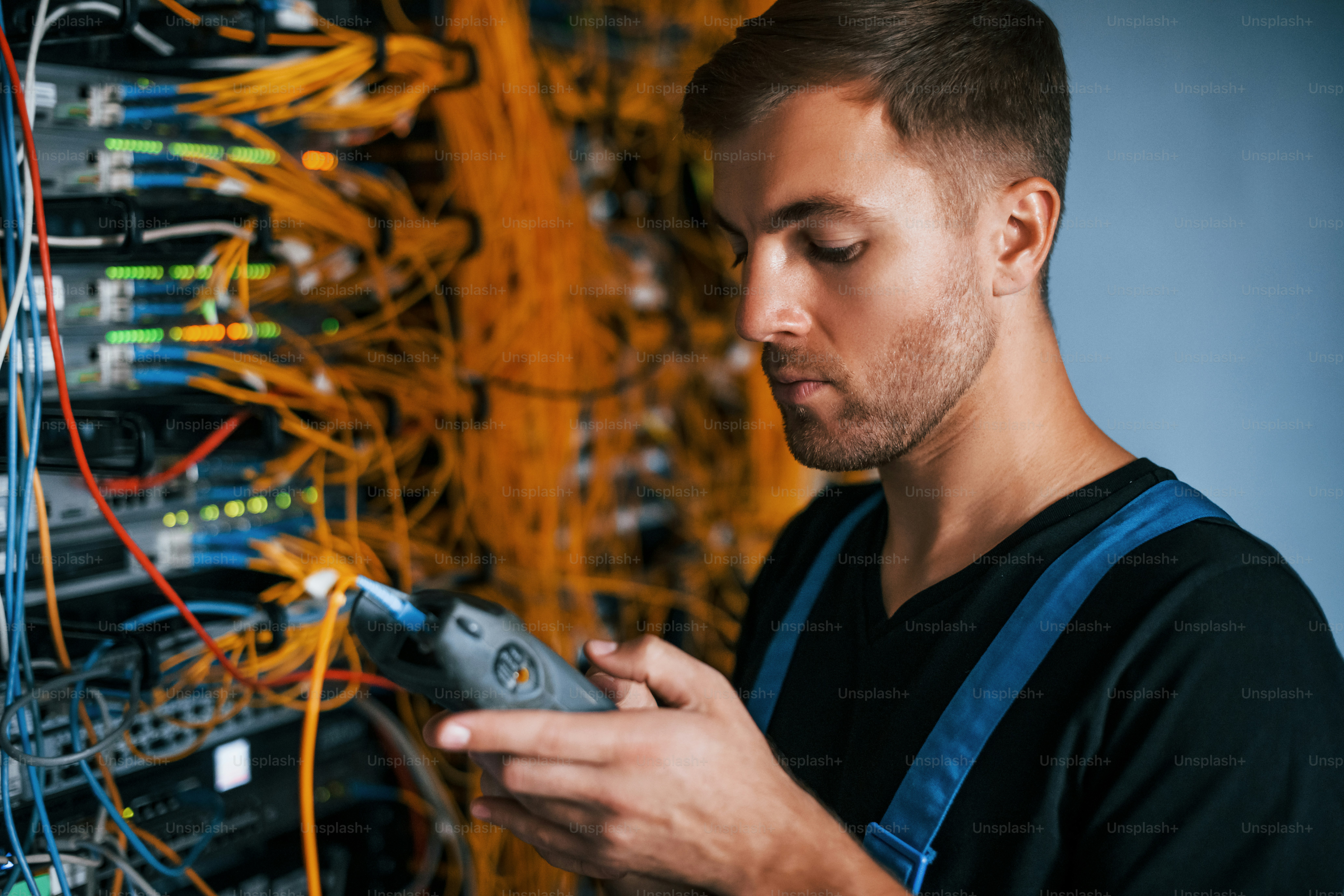 Junger Mann in Uniform hat einen Job mit Internetgeräten und Kabeln im Serverraum.