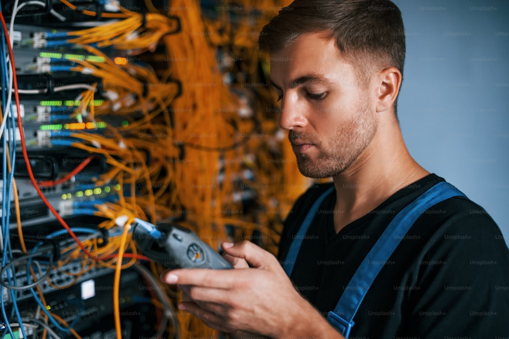 Young man in uniform have a job with internet equipment and wires in server room.