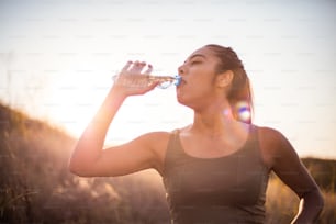 Sporty young woman drinking water outdoors.