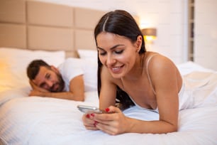 Junges Paar im Bett Ehemann frustriert verärgert und unzufrieden, während seine internetsüchtige Frau Handy in sozialen Netzwerken sucht ignoriert ihn in Beziehung häusliche Probleme