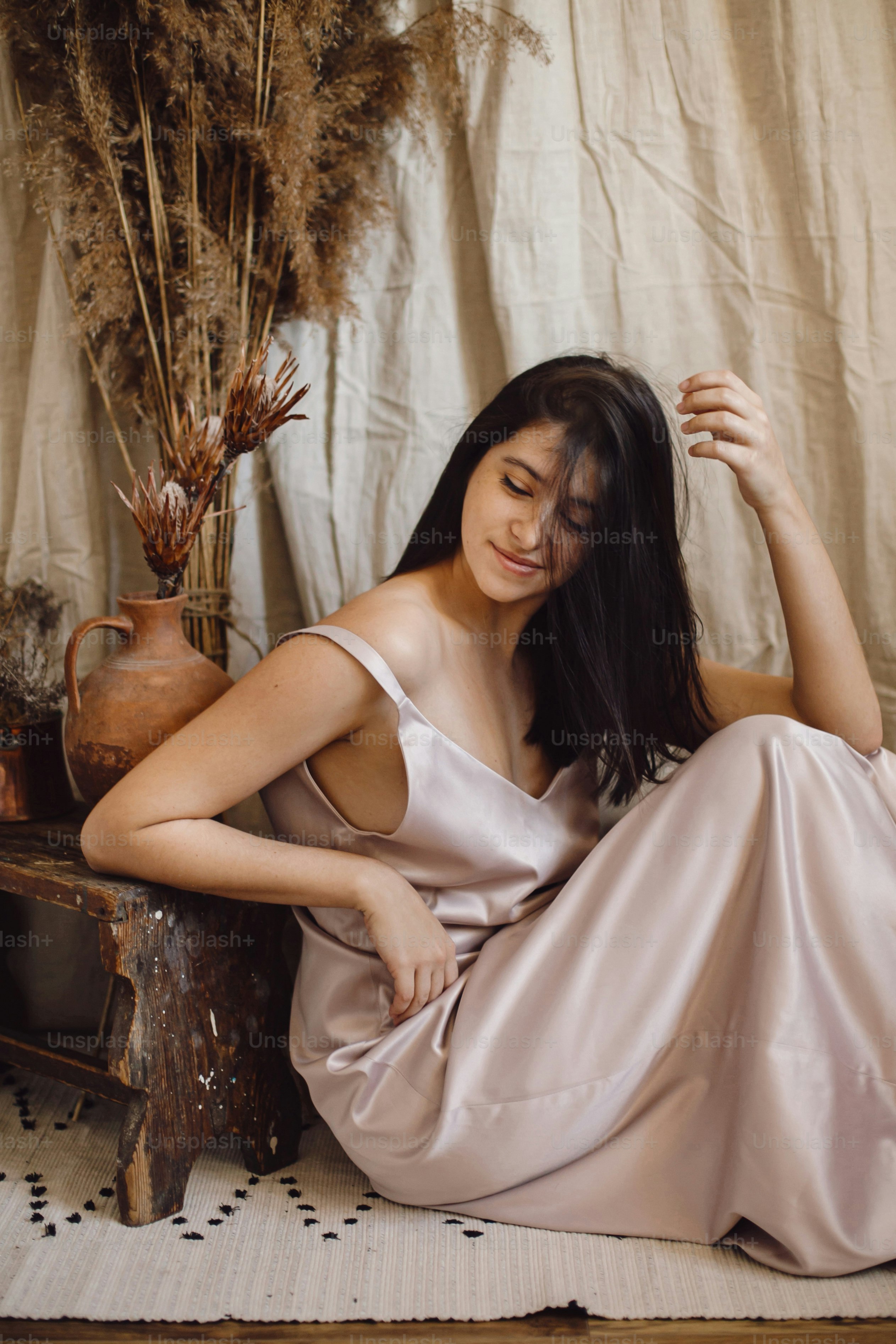 シルクのドレスを着たスタイリッシュでファッショナブルな女性は、ベージュの背景に枯れ草と花のある自由奔放に生きるスタイルの部屋で官能的にポーズをとっています。現代の自由奔放な花嫁。大気のインテリアに若い魅力的な女性