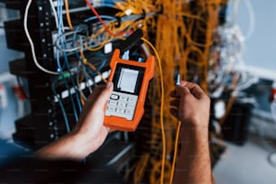 Young man withj measuring device in hands works with internet equipment and wires in server room.