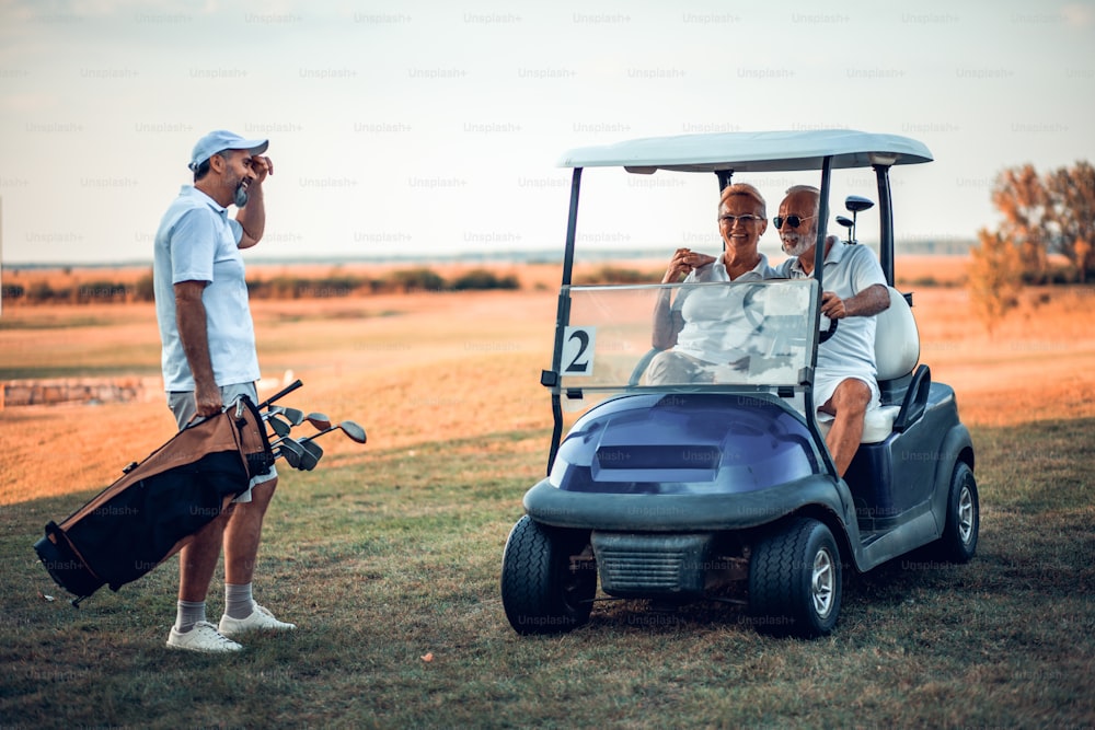 Tre golfisti anziani che parlano. Uomo e donna in golf car.