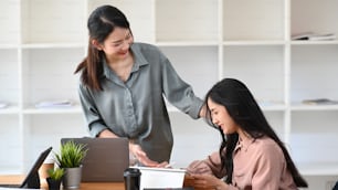 Two young happy female designer talking and working together in creative office.