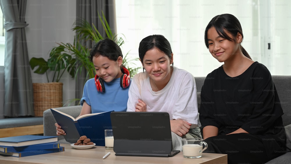 세 명의 어린 소녀들이 거실의 소파에 함께 앉아 디지털 태블릿으로 재미있는 것을 보고 있다.