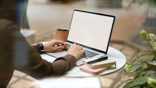 カフェで物資を置いた円卓の上でノートパソコンで作業する女性の手のトリミングショット