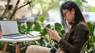 オフィスの庭に座ってリラックスしながらスマートフォンを使用する若い女性労働者の横顔