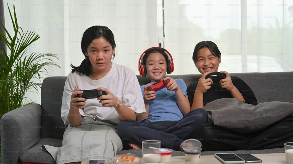 Happy Asian girls playing video games and sitting together on sofa at home.