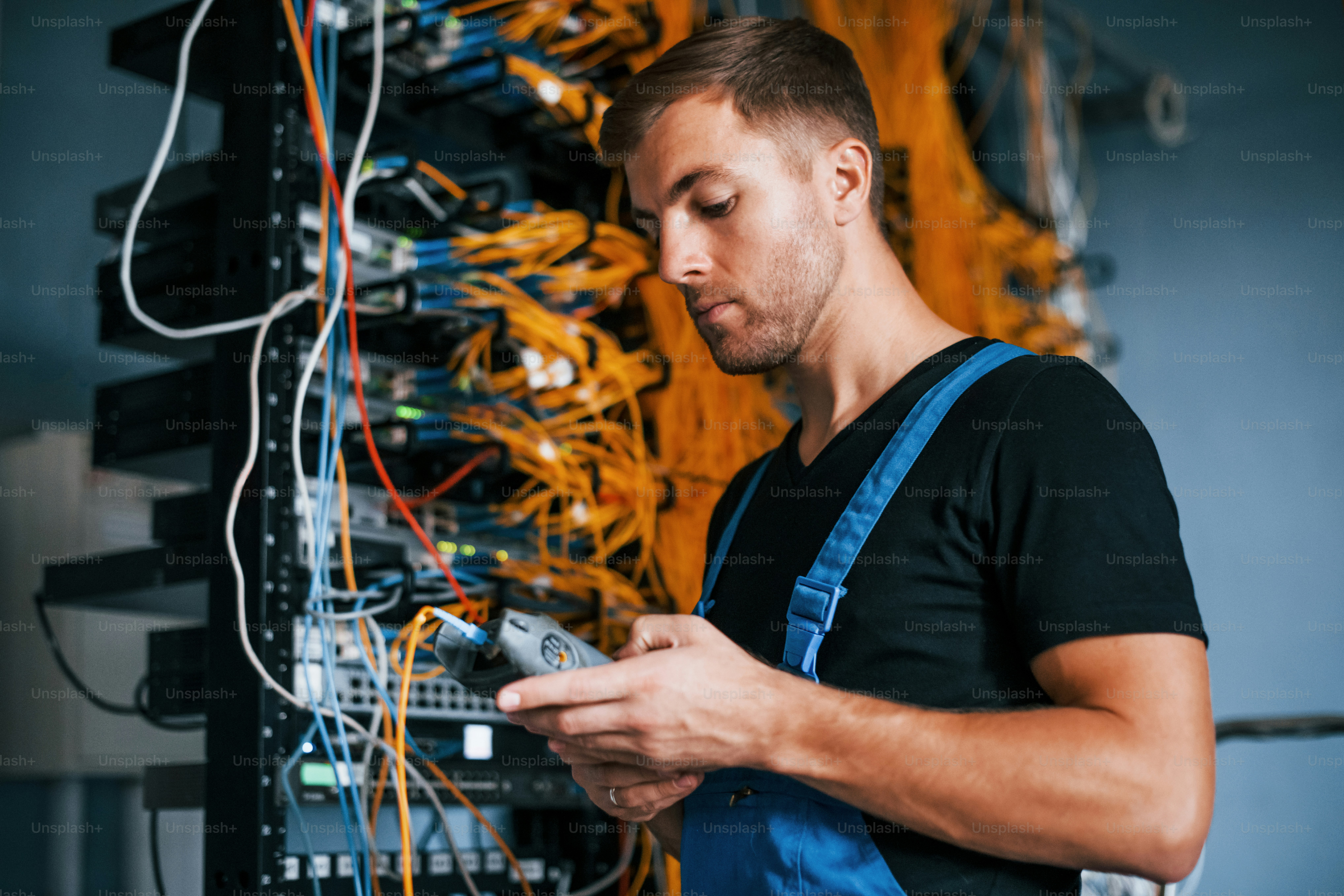 Un joven en uniforme tiene un trabajo con equipos de Internet y cables en la sala de servidores.