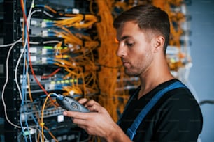 Young man in uniform have a job with internet equipment and wires in server room.