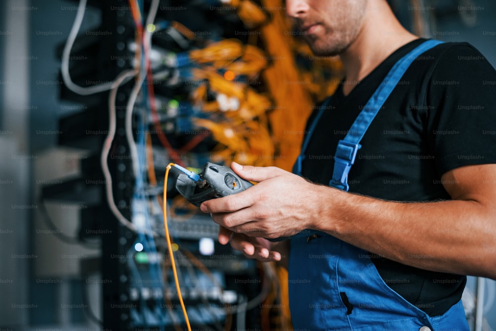 Junger Mann in Uniform hat einen Job mit Internetgeräten und Kabeln im Serverraum.