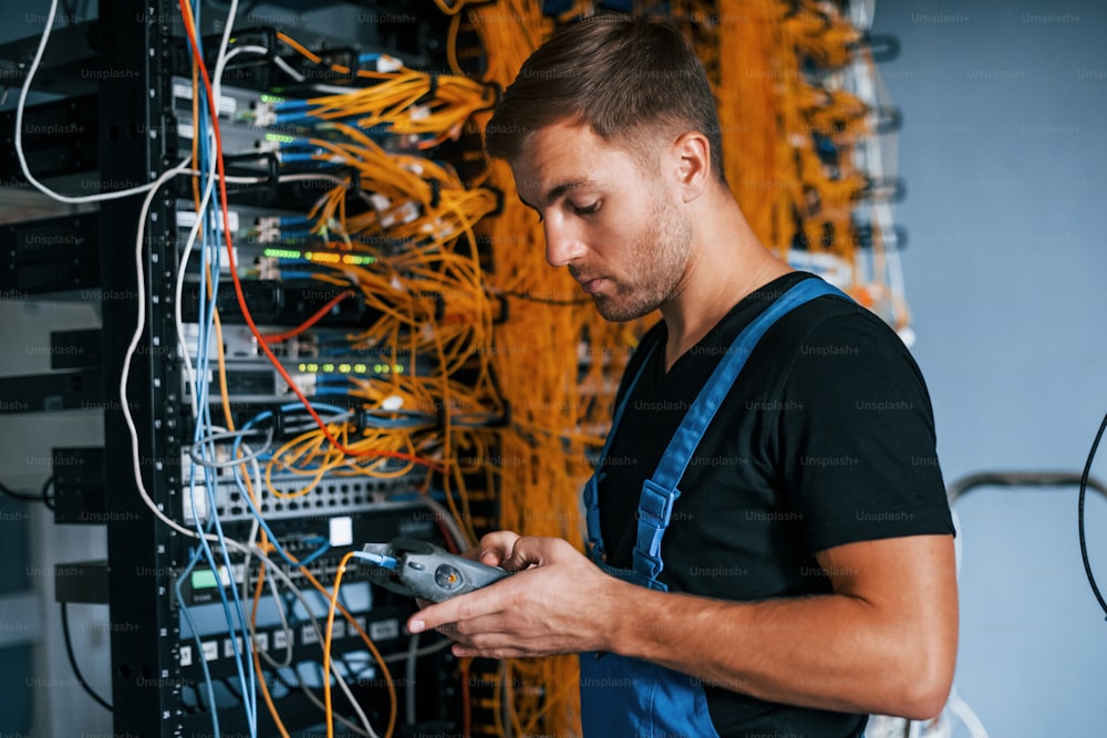 Un joven en uniforme tiene un trabajo con equipos de Internet y cables en la sala de servidores.