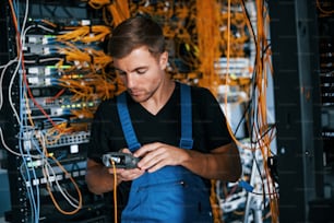 Young man in uniform have a job with internet equipment and wires in server room.