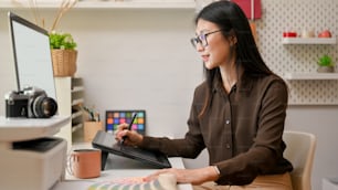 快適なオフィスルームでコンピューターと描画タブレットで作業する女性グラフィックデザイナーの側面図