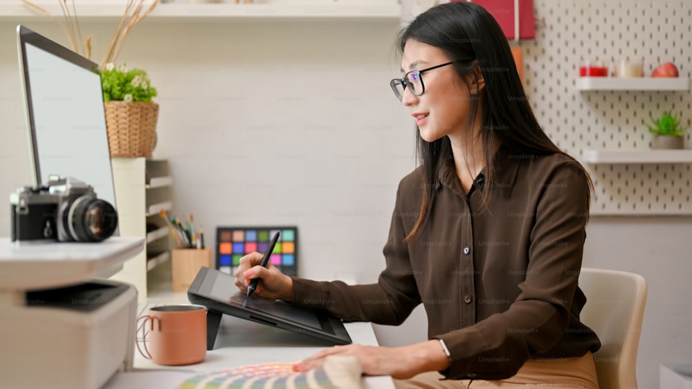 Side view of female graphic designer working on computer and drawing tablet on comfortable office room