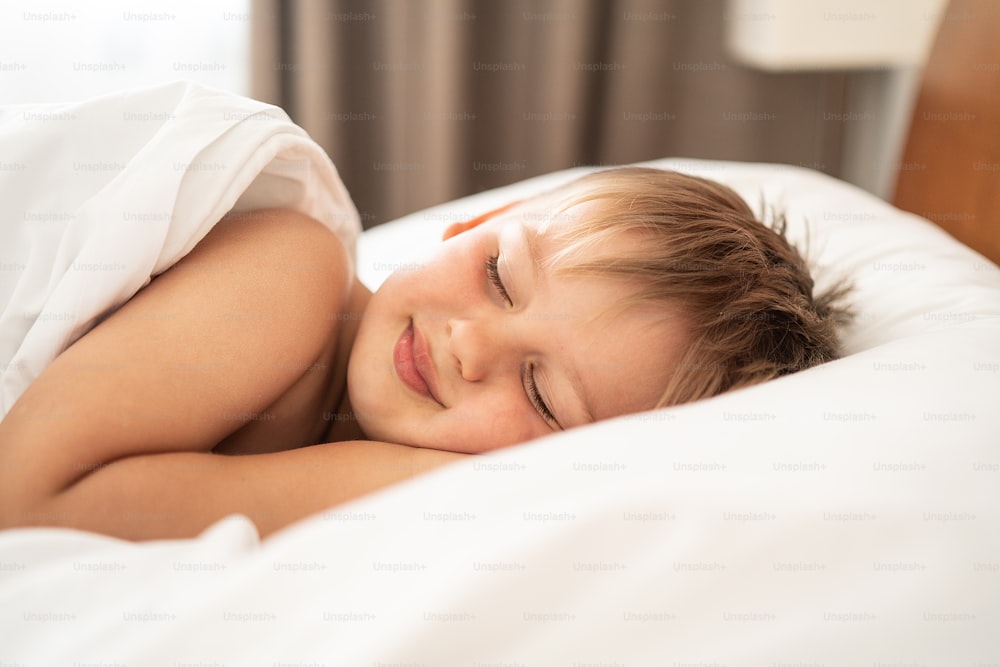 Little boy sleeping in the bed, smiling in his dream. Happy childhood concept.