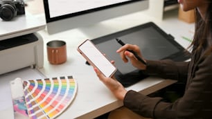 Seitenansicht einer Grafikdesignerin mit Mock-up-Smartphone während des Sitzens am Büroschreibtisch, Clipping-Pfad