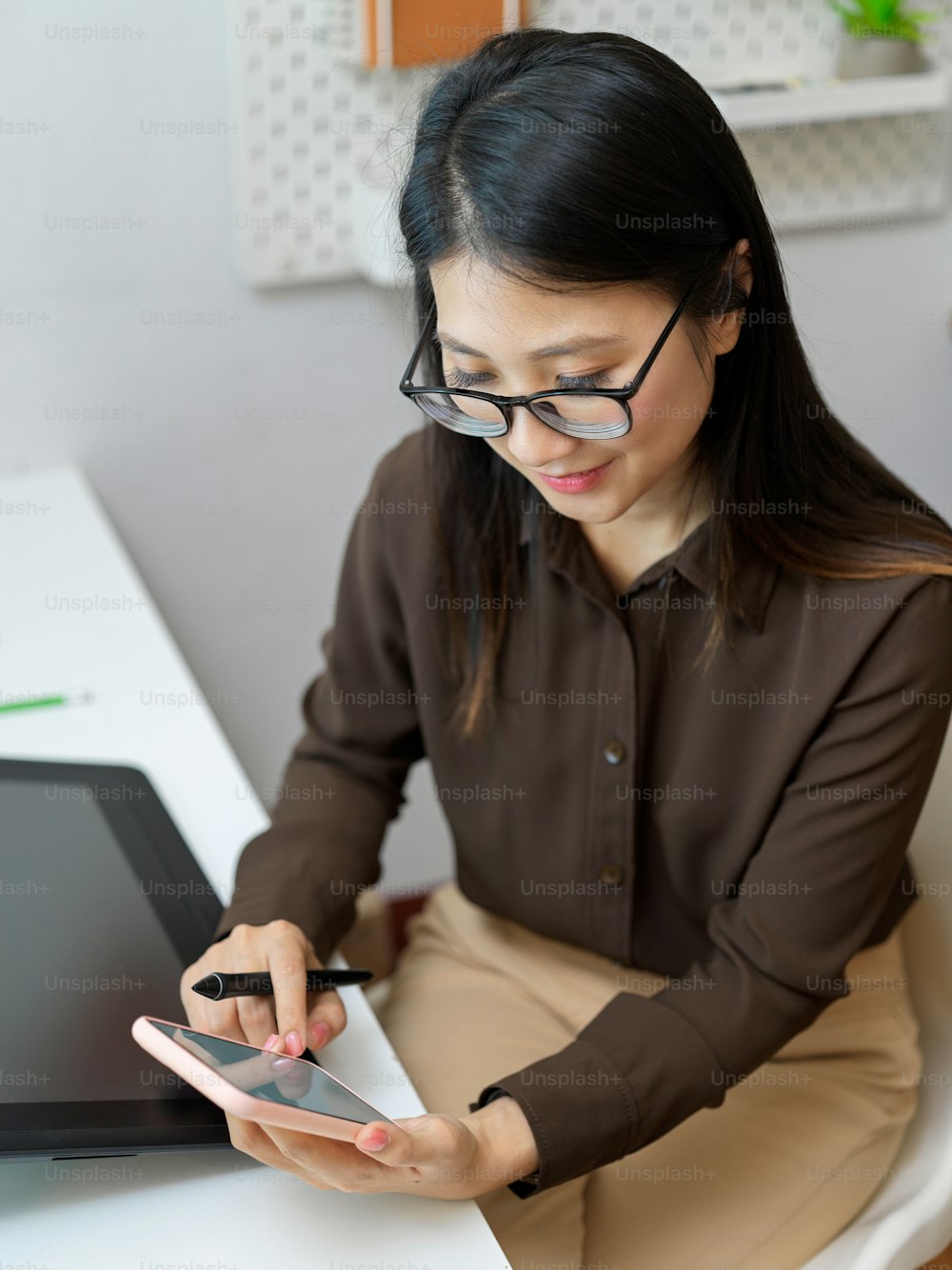Top view of female office worker with eyeglasses using smartphone while sitting at office desk
