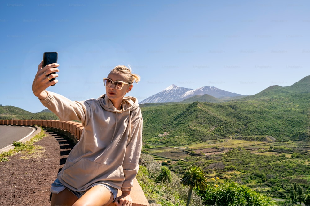 Mujer joven tomando selfie o vlogueando en el teléfono móvil durante su viaje en la isla. Estilo de vida, viajes y concepto de influencia social.