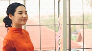 Business people work on project planning board in office and having conversation with coworker friend to analyze project development . They use sticky notes posted on glass wall to make it organized .