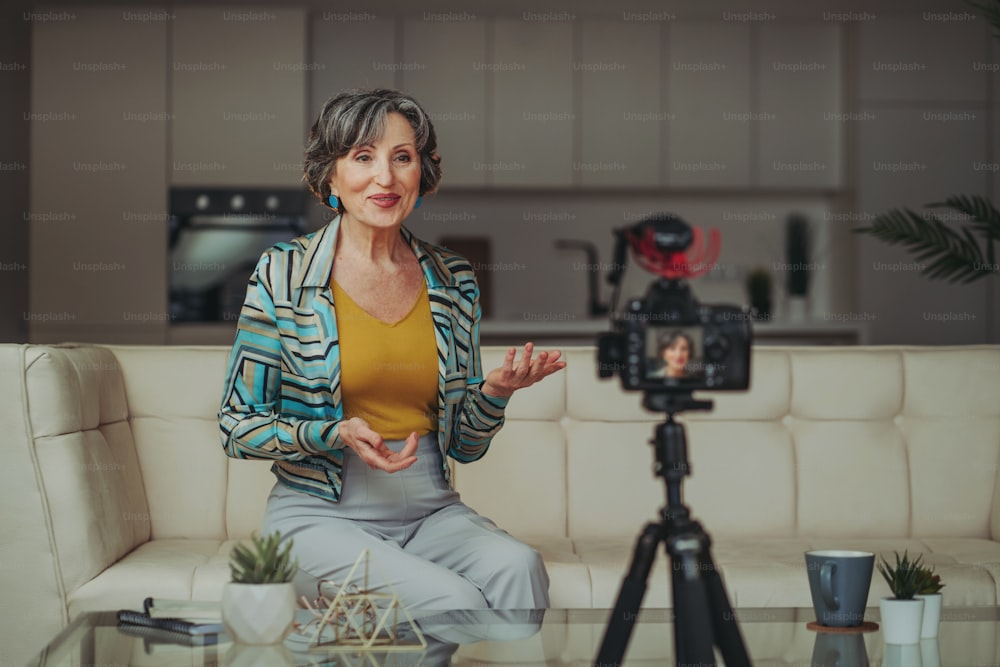 Elegante mujer mayor que hace contenido de video usando una cámara en su sala de estar. Concepto de redes sociales.