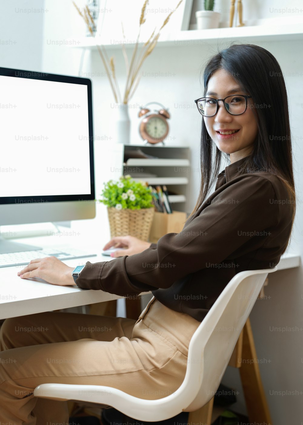 Cropped shot of female office worker with eyeglasses smiling to camera while sitting in home office room