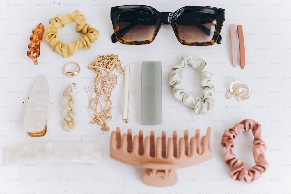 Disposition moderne des accessoires d’été. Bijoux dorés, lunettes de soleil, pinces à cheveux et bandeaux, barrettes sur table blanche. Des essentiels féminins. Accessoires colorés bohèmes