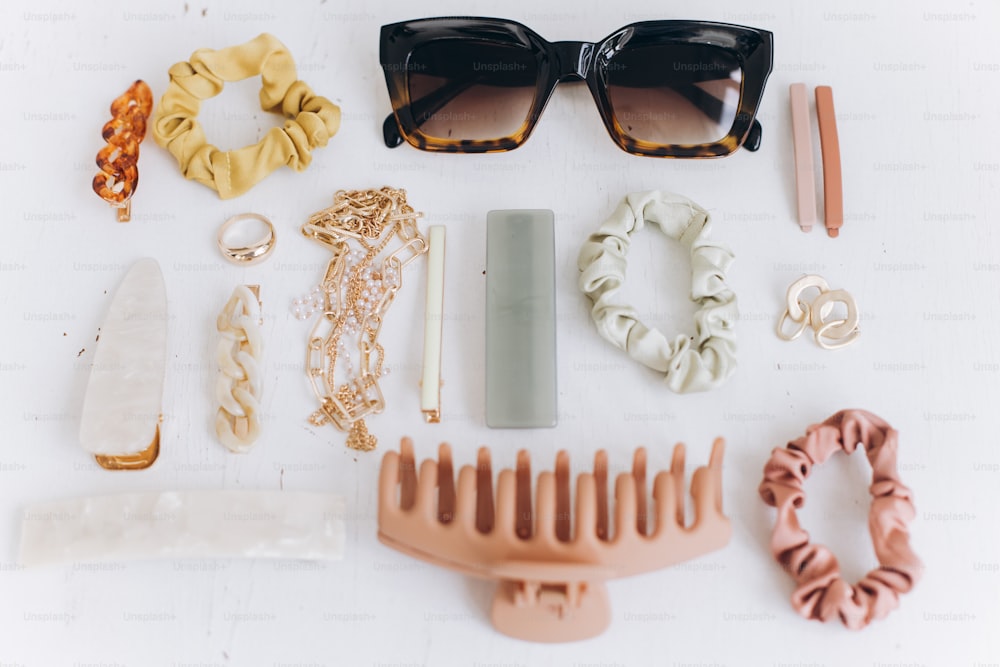 Modern summer accessories layout. Golden jewellery, sunglasses, hair clips and hairbands, barrettes on white table top view. Feminine essentials. Boho colorful accessories