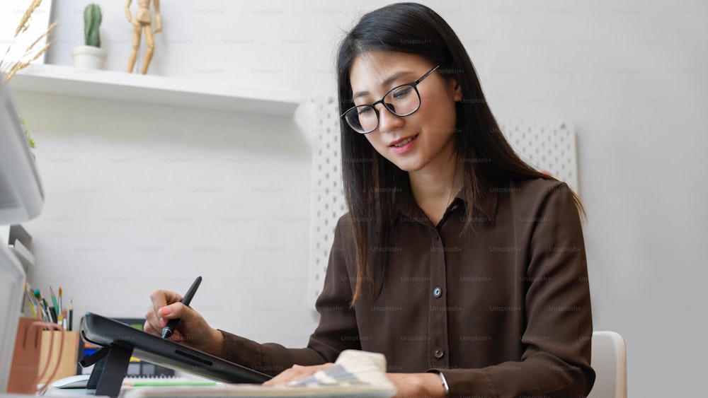 Half-length portrait of female graphic designer smiling while working with drawing tablet and colour swatch