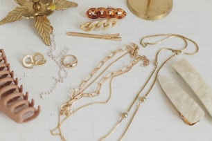 Modern golden jewellery and hair clips on white wooden table with vintage candlesticks. Stylish gold ring, chain necklace, earrings, beige hairpins and barrettes. Boho accessories
