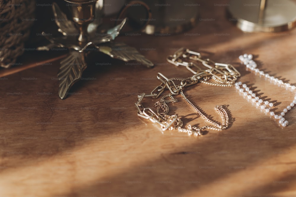 ヴィンテージの燭台とテーブルの上にはモダンなゴールドとパールのアクセサリー。日当たりの良い光の中で木製の背景にスタイリッシュな金色のネックレスとリング。
