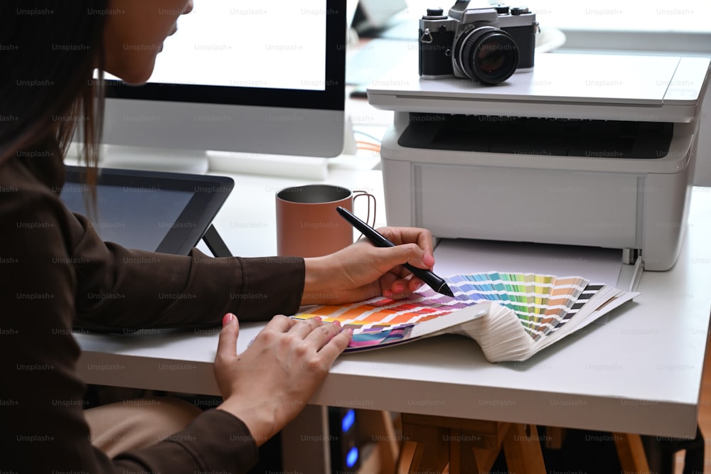 Plan recadré d’un jeune graphiste travaillant avec une tablette graphique à l’aide d’échantillons de couleurs au bureau de création.