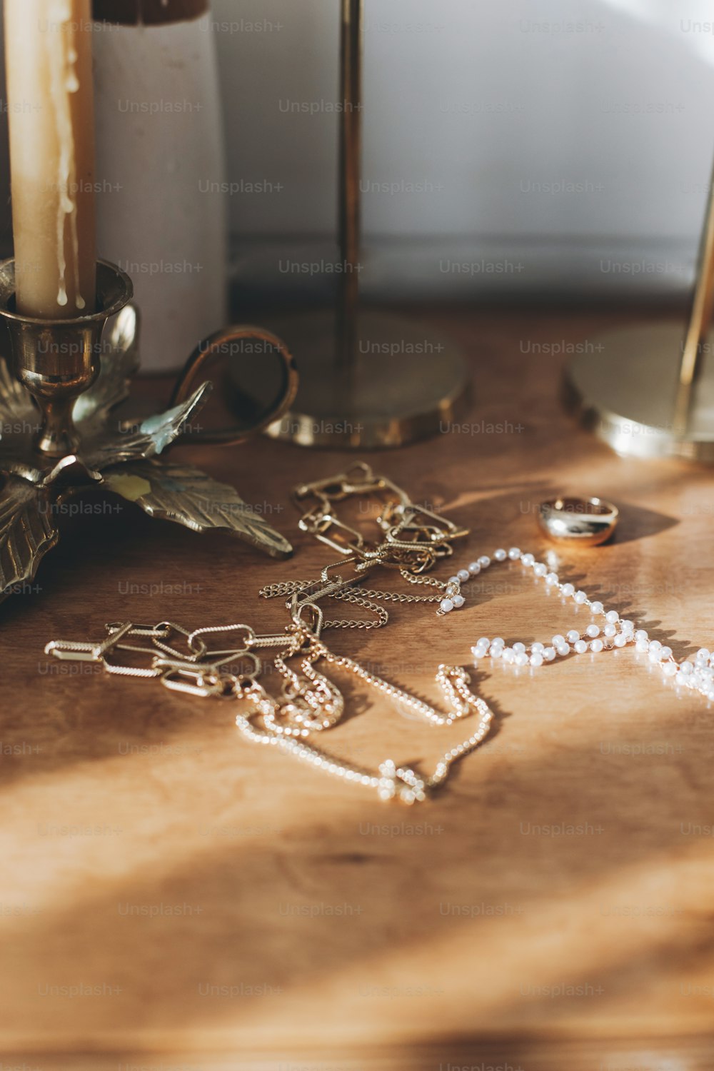 Acessórios modernos de ouro e pérola na mesa com castiçais vintage. Colar dourado elegante e anel no fundo de madeira na luz ensolarada.
