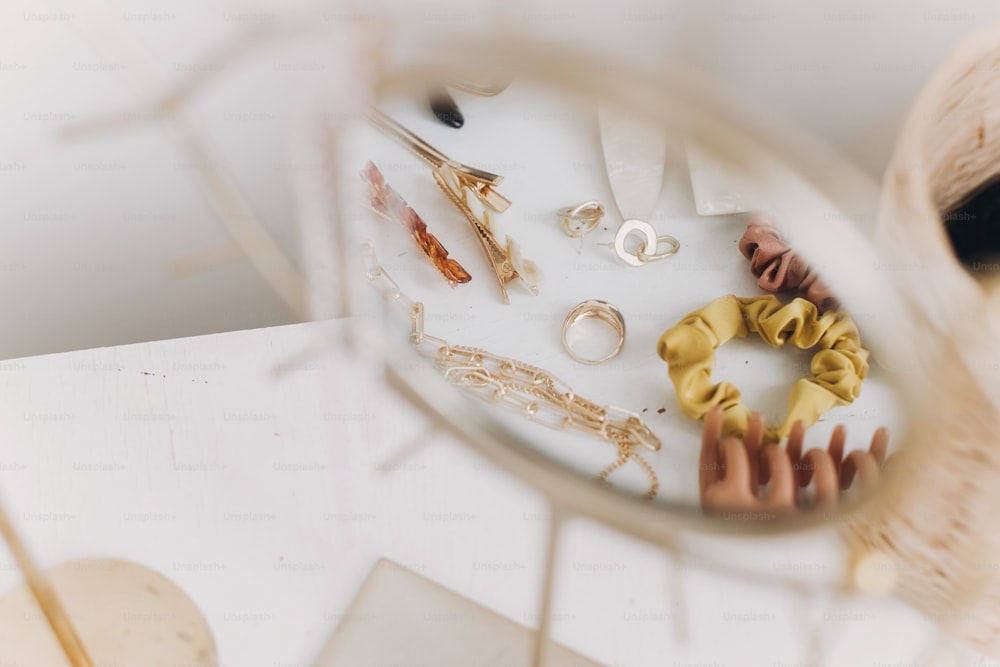 현대적인 황금 보석, 헤어 클립 및 헤어 밴드는 빈티지 양초가있는 흰색 테이블의 보헤미안 거울에 반영됩니다. 세련된 골드 링, 목걸이, 귀걸이, 머리핀, 바렛. 여름 보호 액세서리