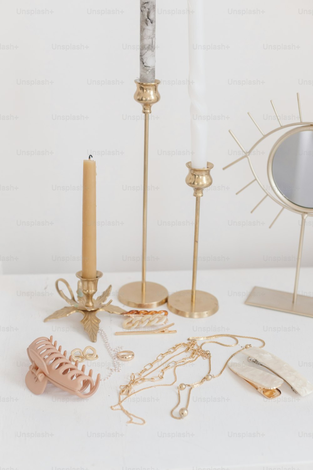 Boho accessories, interior details. Modern golden jewellery, hair clips on white table with vintage candles and boho mirror. Stylish gold ring, chain necklace, earrings, hairpins and barrettes.