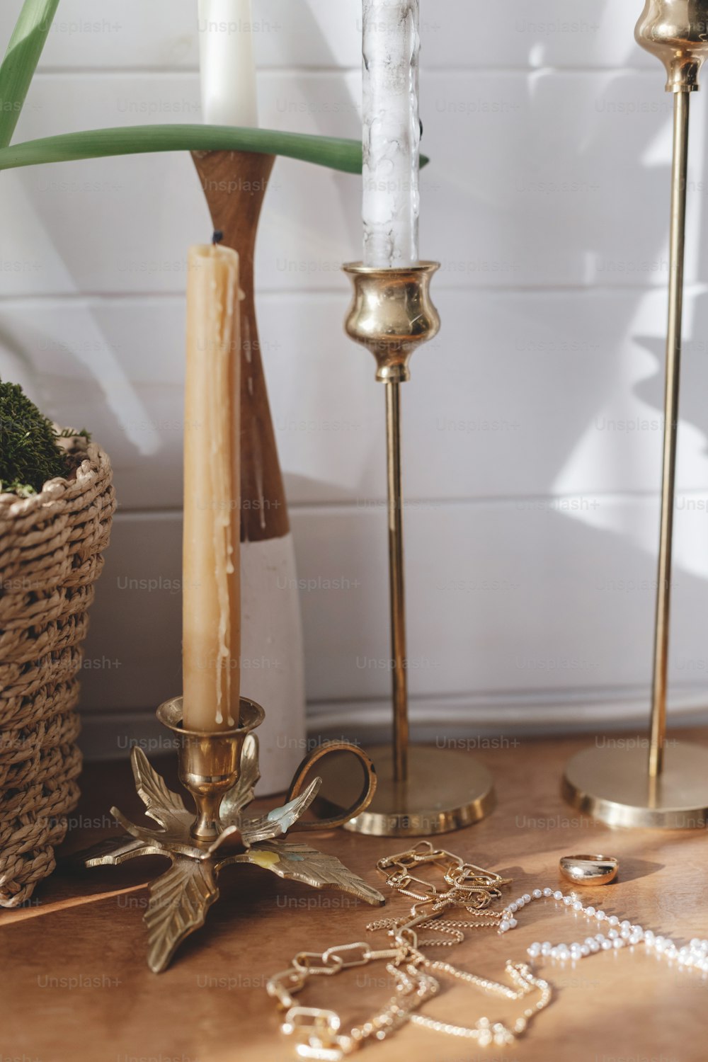 Accessori moderni in oro e perle su tavola con candelieri vintage. Elegante collana e anello d'oro su sfondo di legno in luce soleggiata.