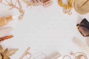 Feminine summer essentials flat lay, space for text. Gold jewellery, sunglasses, hair clips, barrettes, cosmetics on white table with vintage candles. Modern boho accessories