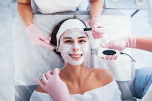 Vue rapprochée d’une femme allongée dans un salon de spa et ayant une procédure de nettoyage du visage par différents appareils et masque.