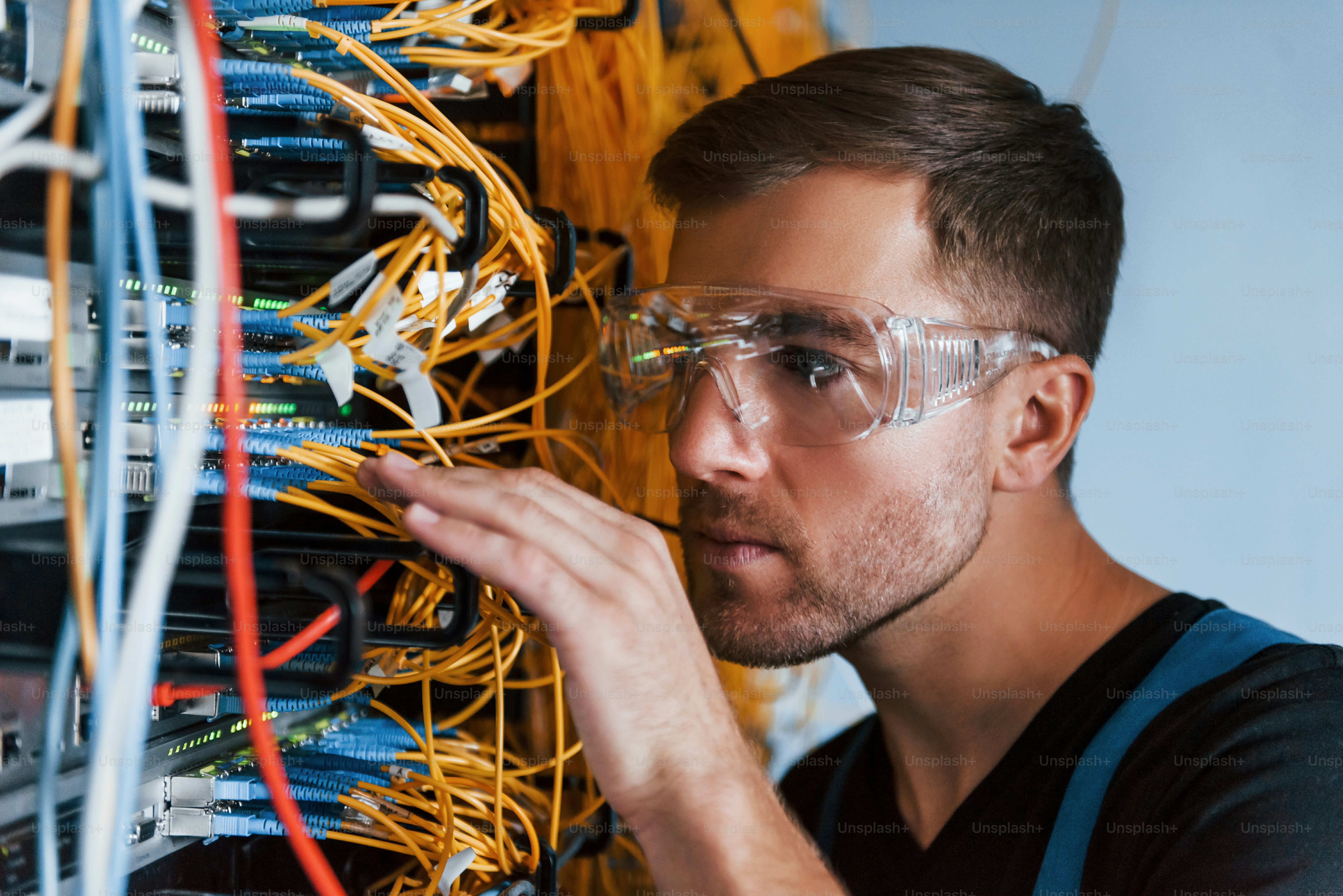 Un joven con gafas protectoras trabaja con equipos de Internet y cables en la sala de servidores.