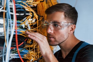 Jovem de óculos de proteção trabalha com equipamentos de internet e fios na sala de servidores.