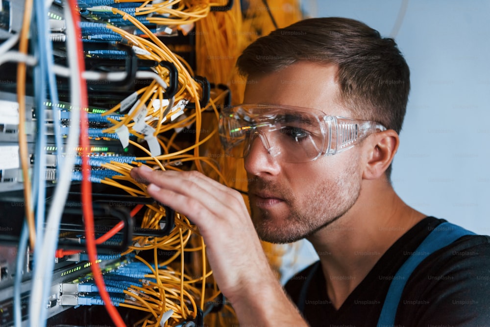 Il giovane in occhiali protettivi lavora con apparecchiature internet e fili nella sala server.