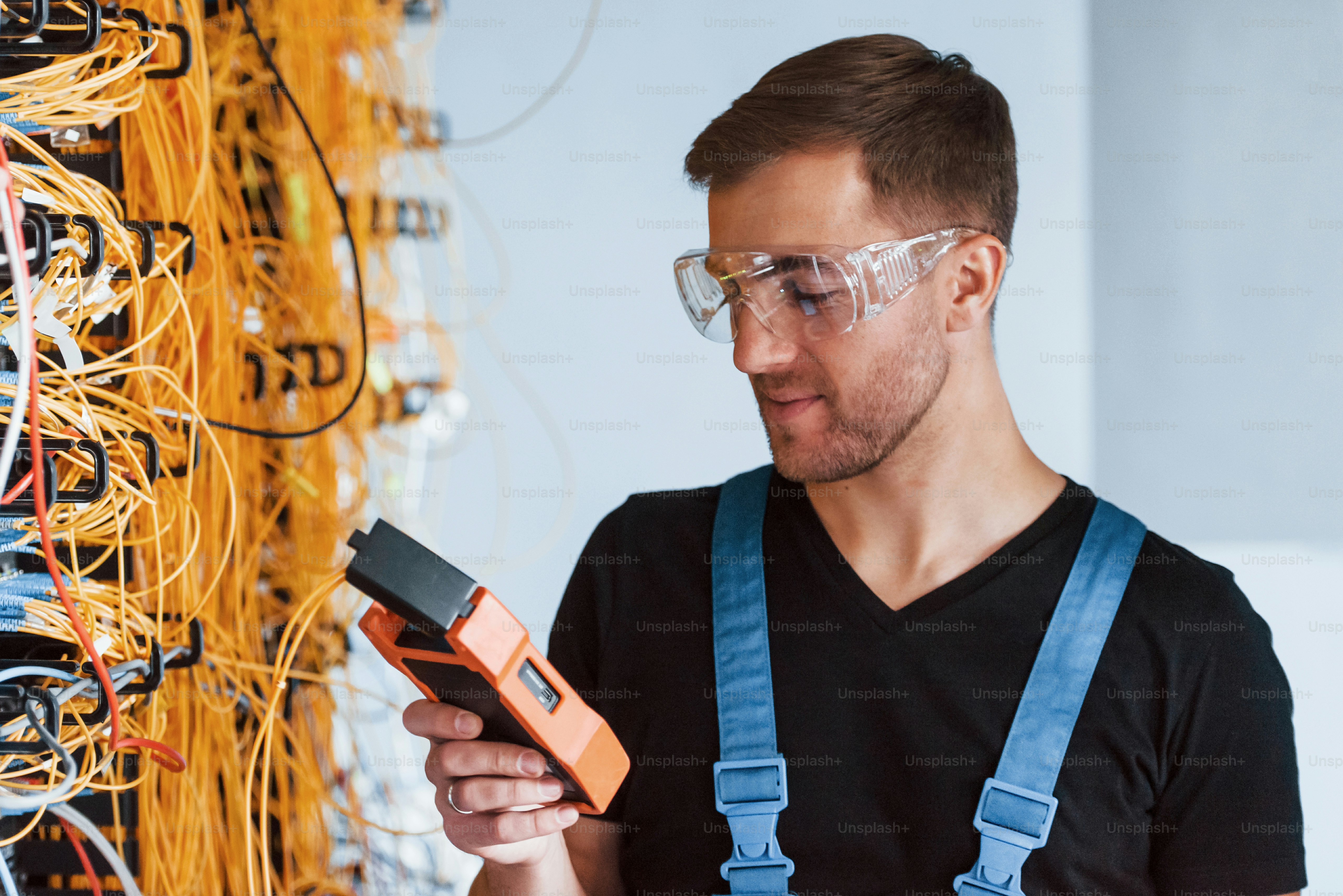 Young man in protective glasses works with internet equipment and wires in server room.