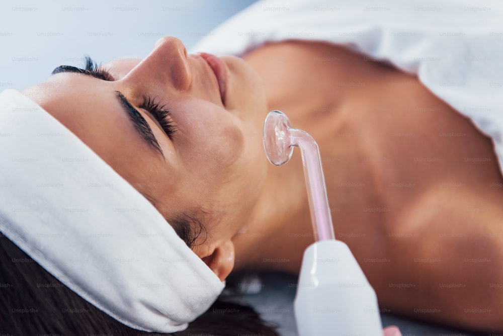 Close up view of woman that lying down in spa salon and have face cleaning procedure by using modern device.