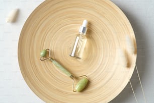 Face massage roller and serum on plate in bathroom. Flat lay, top view. SPA natural organic cosmetics for personal hygiene