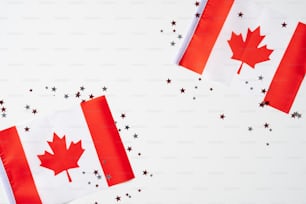 Cartel de Feliz Día de Canadá. 1 de julio. Banderas canadienses con hojas de arce y confeti sobre fondo blanco.
