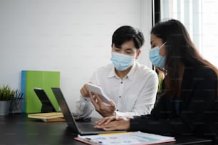 Dois empresários usando máscara de proteção usando calculadora e trabalhando juntos no escritório.