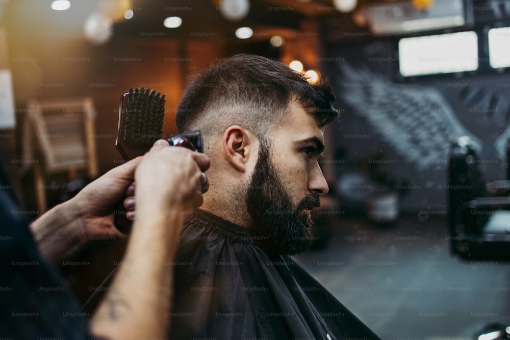 Good looking young adult man getting a hair and beard styling and dressing treatment by professional hairstylist.