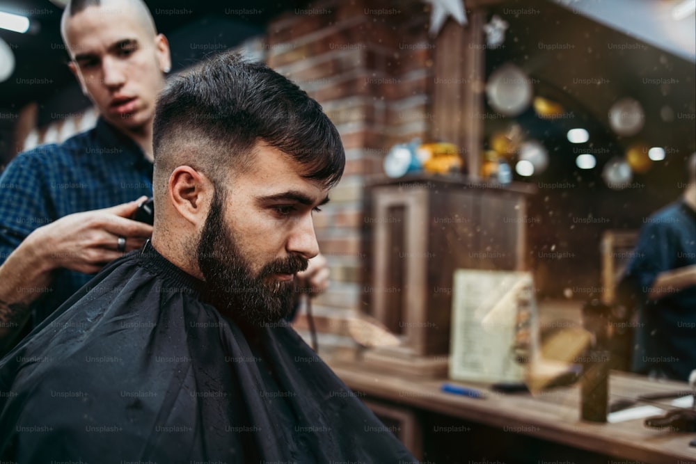 Good looking young adult man getting a hair and beard styling and dressing treatment by professional hairstylist.